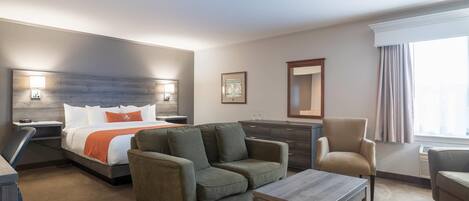 A hotel room with a bed, two sofas, a coffee table, a desk, and a dresser.