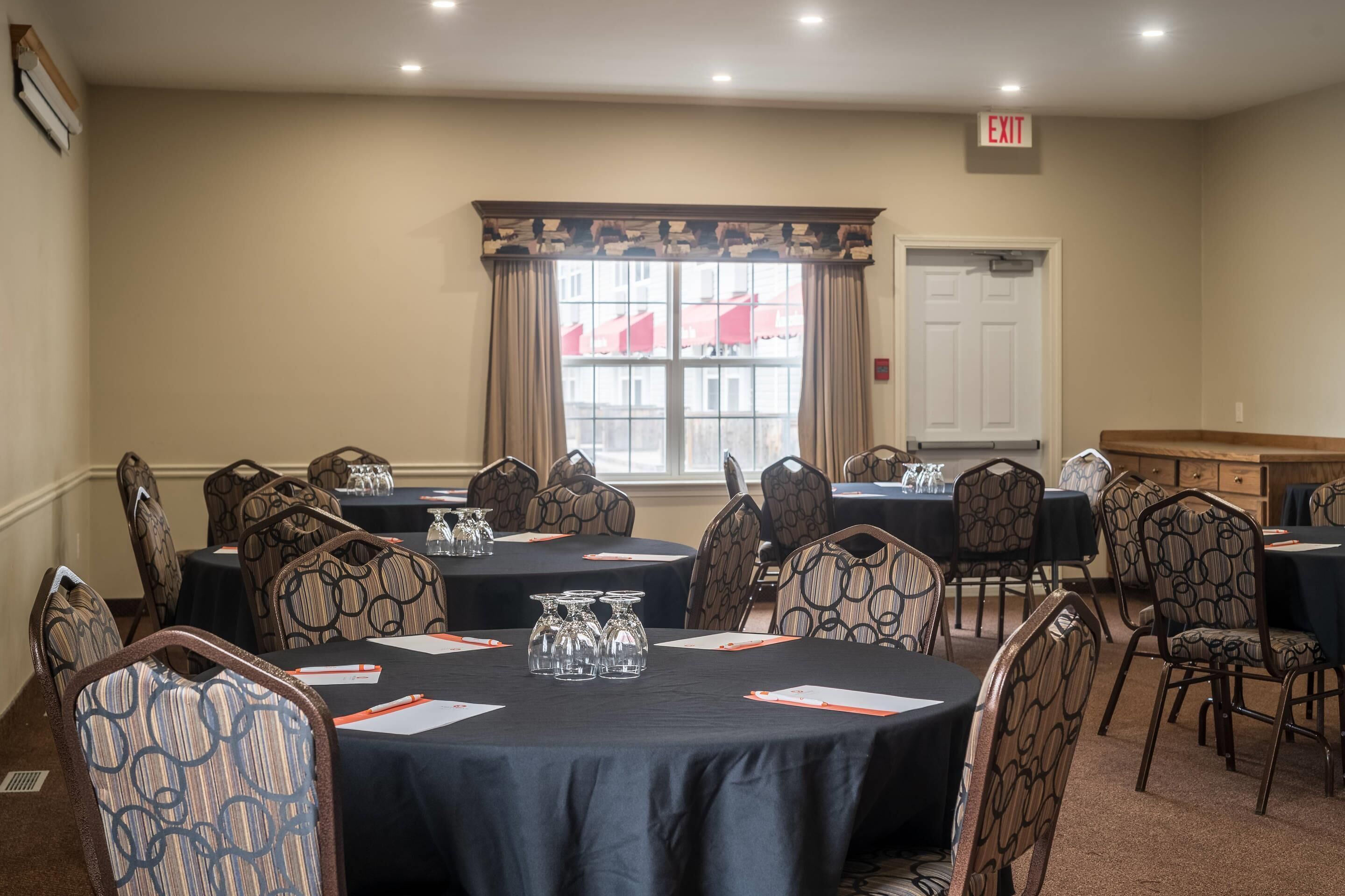 A conference room with round tables, patterned chairs, and a large window with curtains.