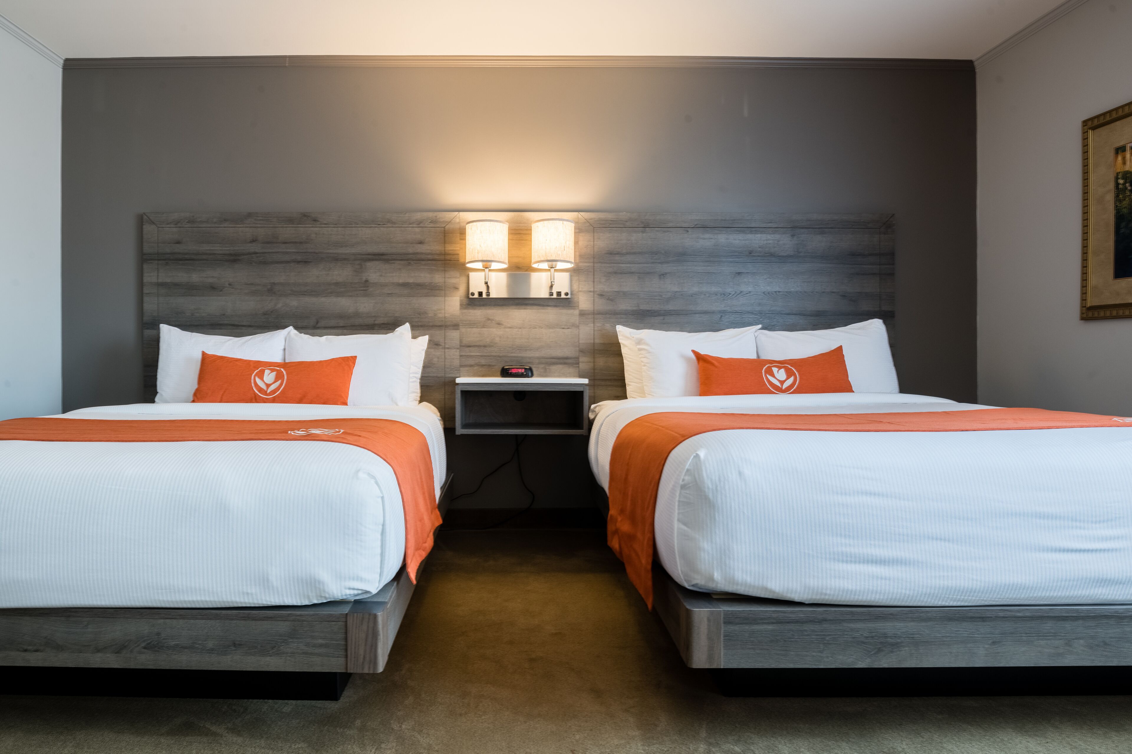 Ein Hotelzimmer mit zwei Betten, jeweils mit weißer Bettwäsche und orangefarbenen Akzenten, einem Nachttisch mit Lampe und einem Holzkopfteil.