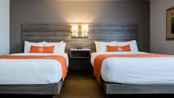 Ein Hotelzimmer mit zwei Betten, jeweils mit weißer Bettwäsche und orangefarbenen Akzenten, einem Nachttisch mit Lampe und einem Holzkopfteil.