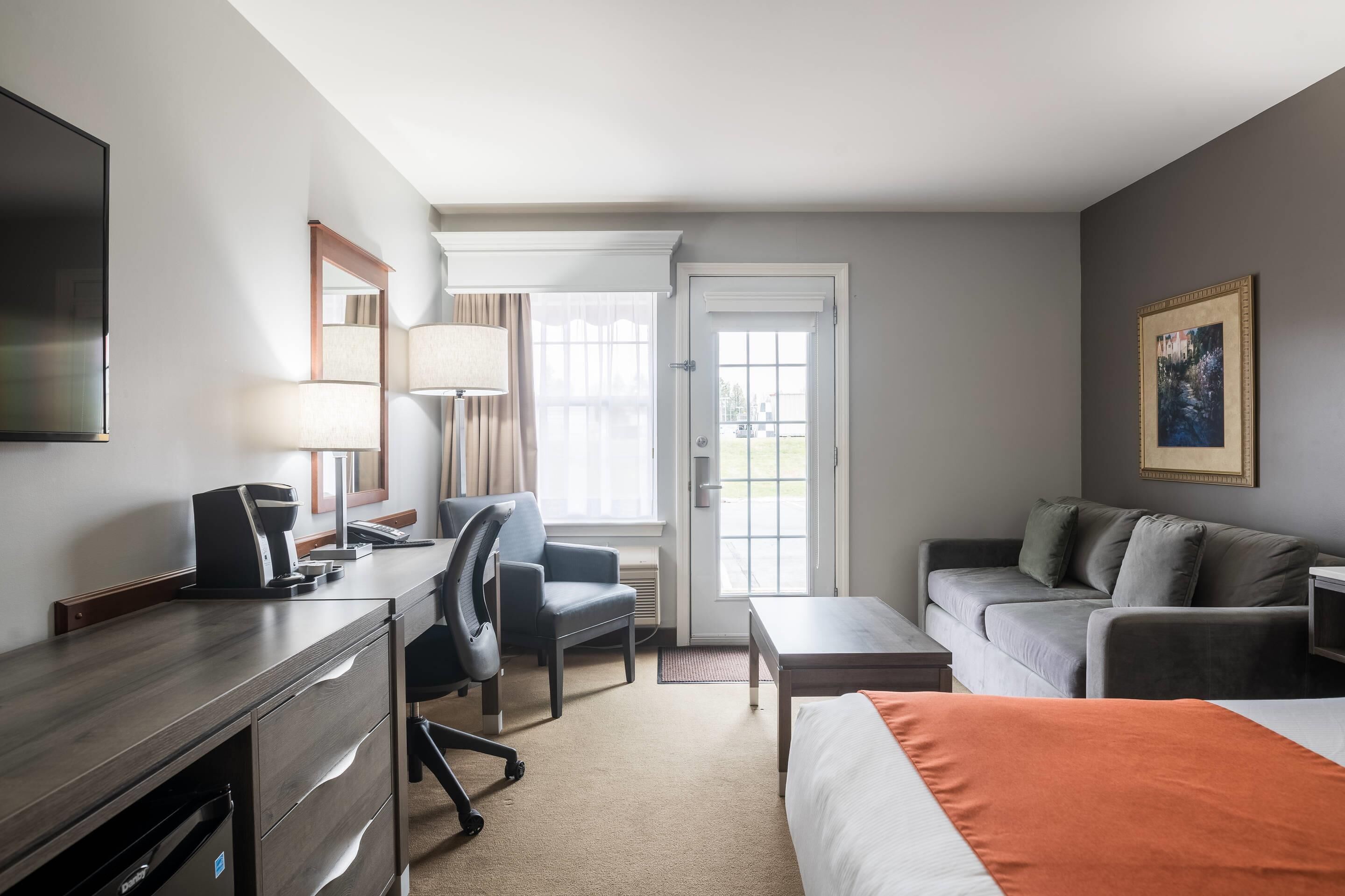 A hotel room with a bed, desk, chair, sofa, and a painting on the wall.