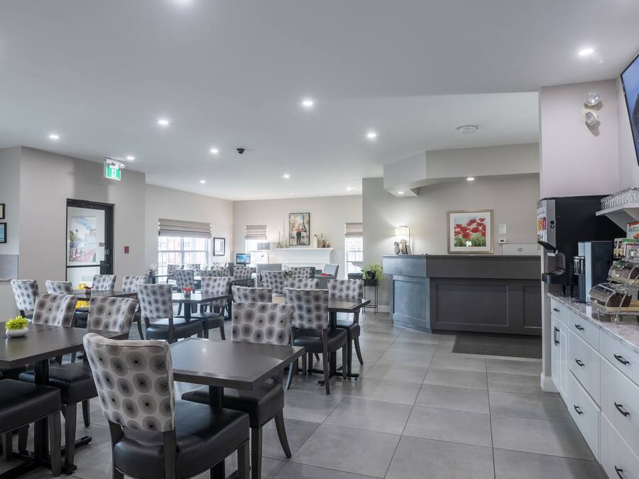 A spacious restaurant with multiple tables and chairs, a counter with a display case, and a television mounted on the wall.