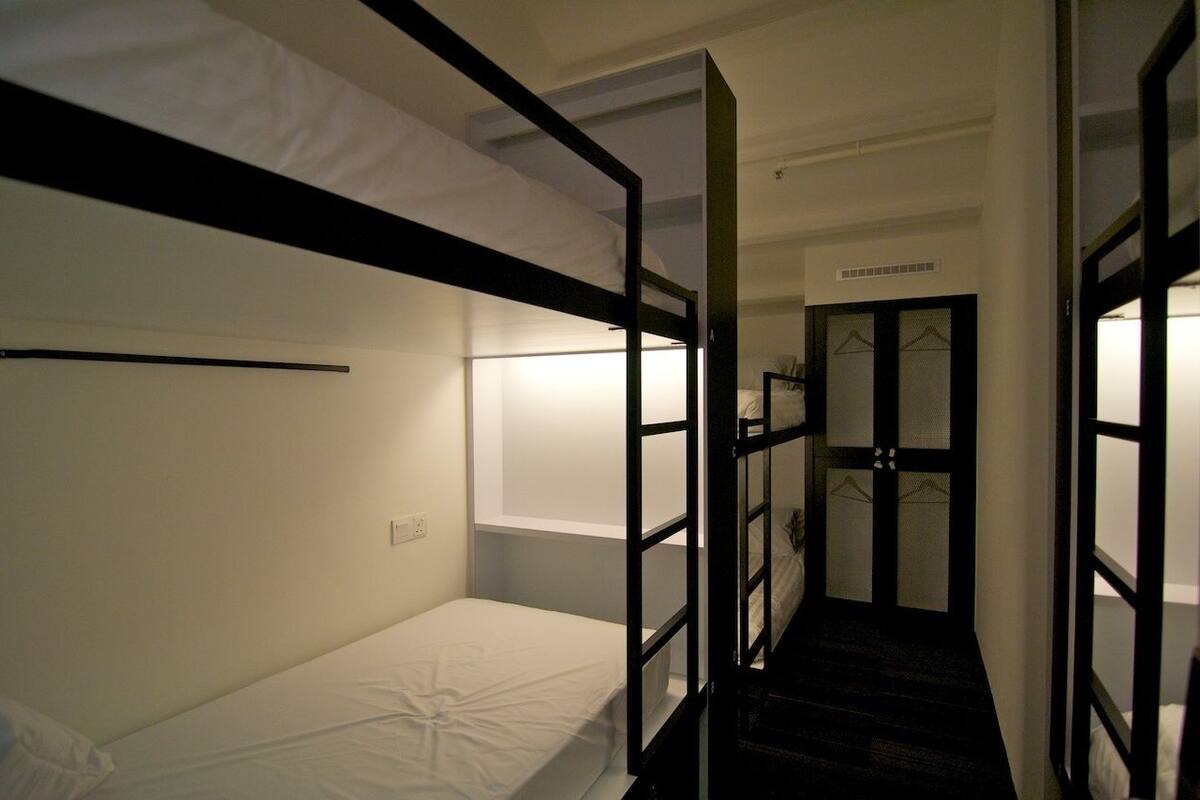 A dormitory-style room with bunk beds, a small desk, and a window.