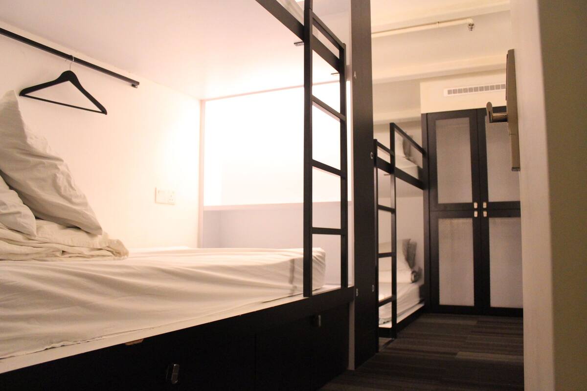 A single bed with a white mattress and a black frame, a hanging garment, and a door with a frosted glass panel.