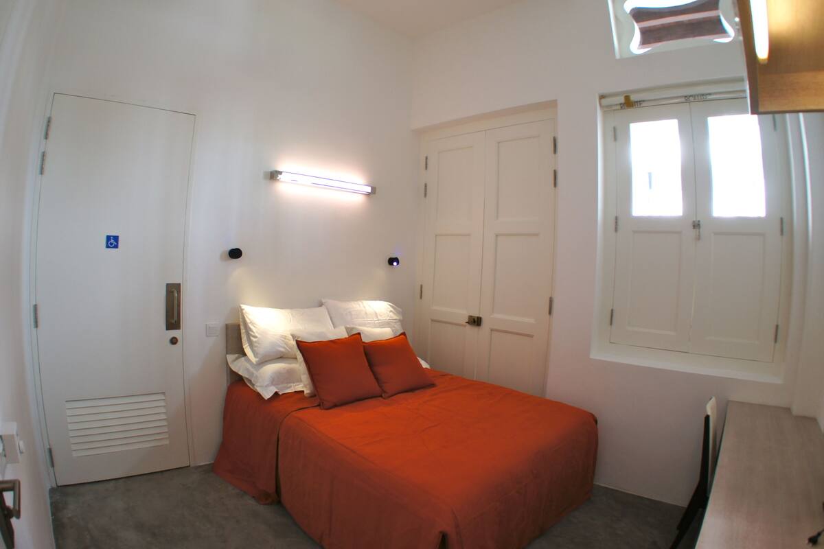 A bedroom with a bed, a desk, and a window.