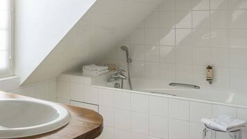Un baño moderno con una bañera independiente, un mueble de tocador de madera y suelo de baldosas.