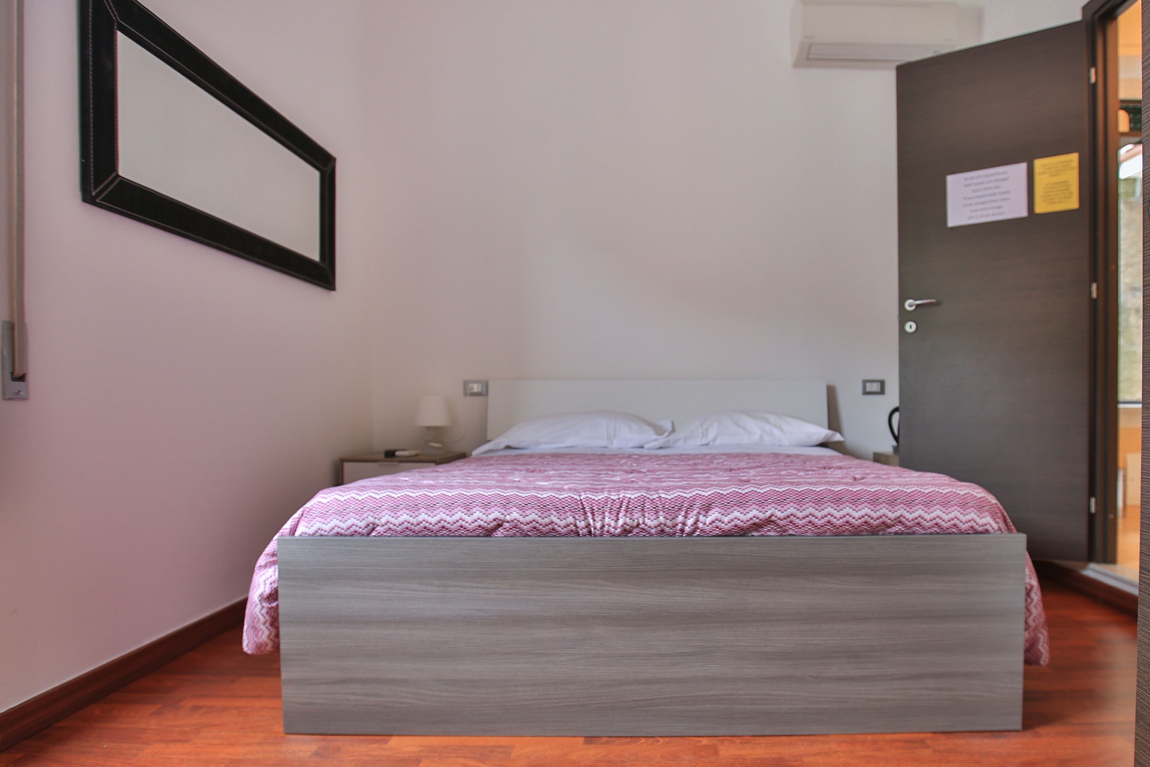 Une chambre à coucher avec un lit, une table de chevet, un miroir fixé au mur et une porte avec une pancarte.