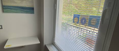 A room with a window, a painting on the wall, and a small shelf.
