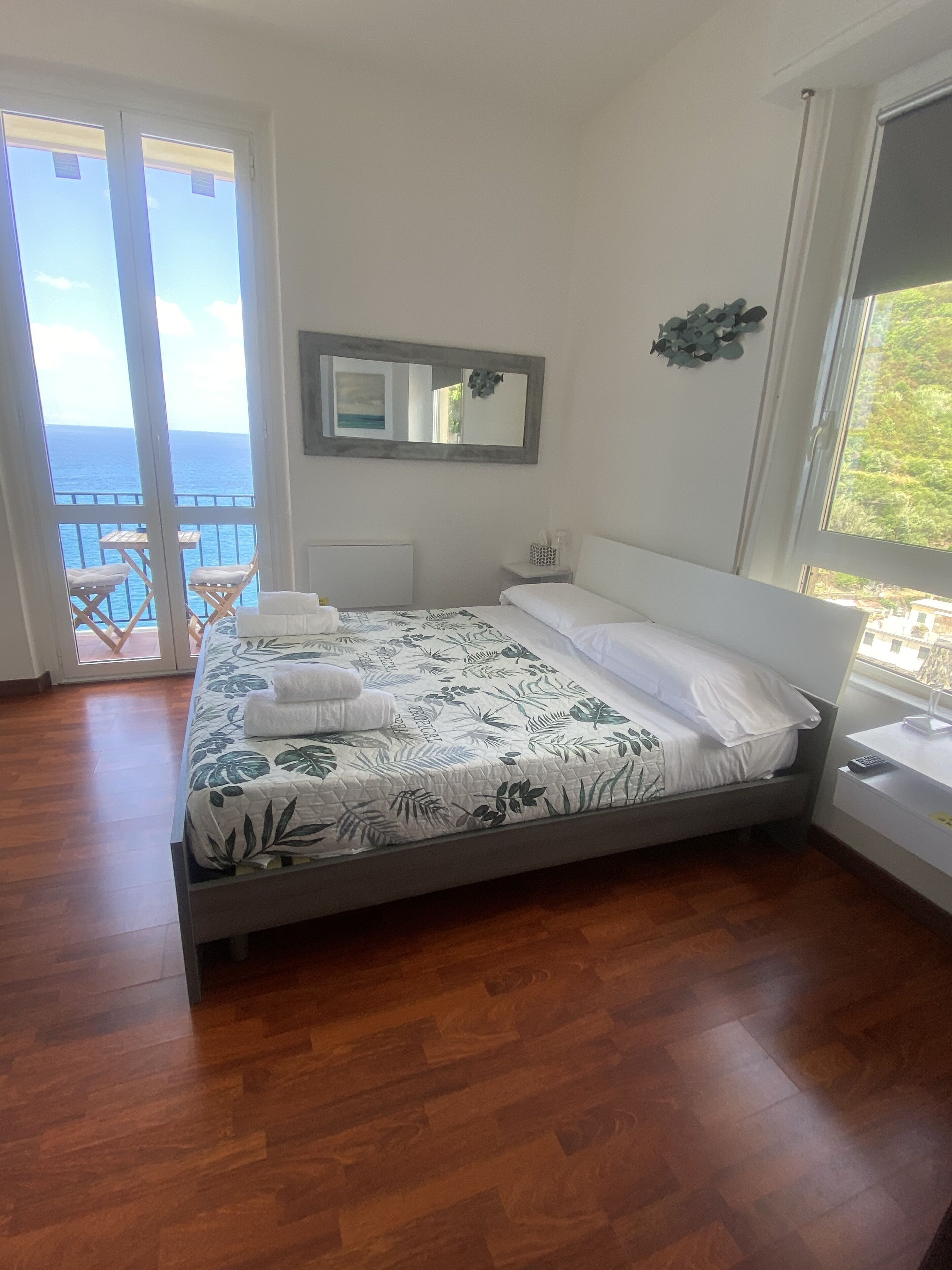 Ein Schlafzimmer mit Bett, Fenster, Spiegel und Meerblick.