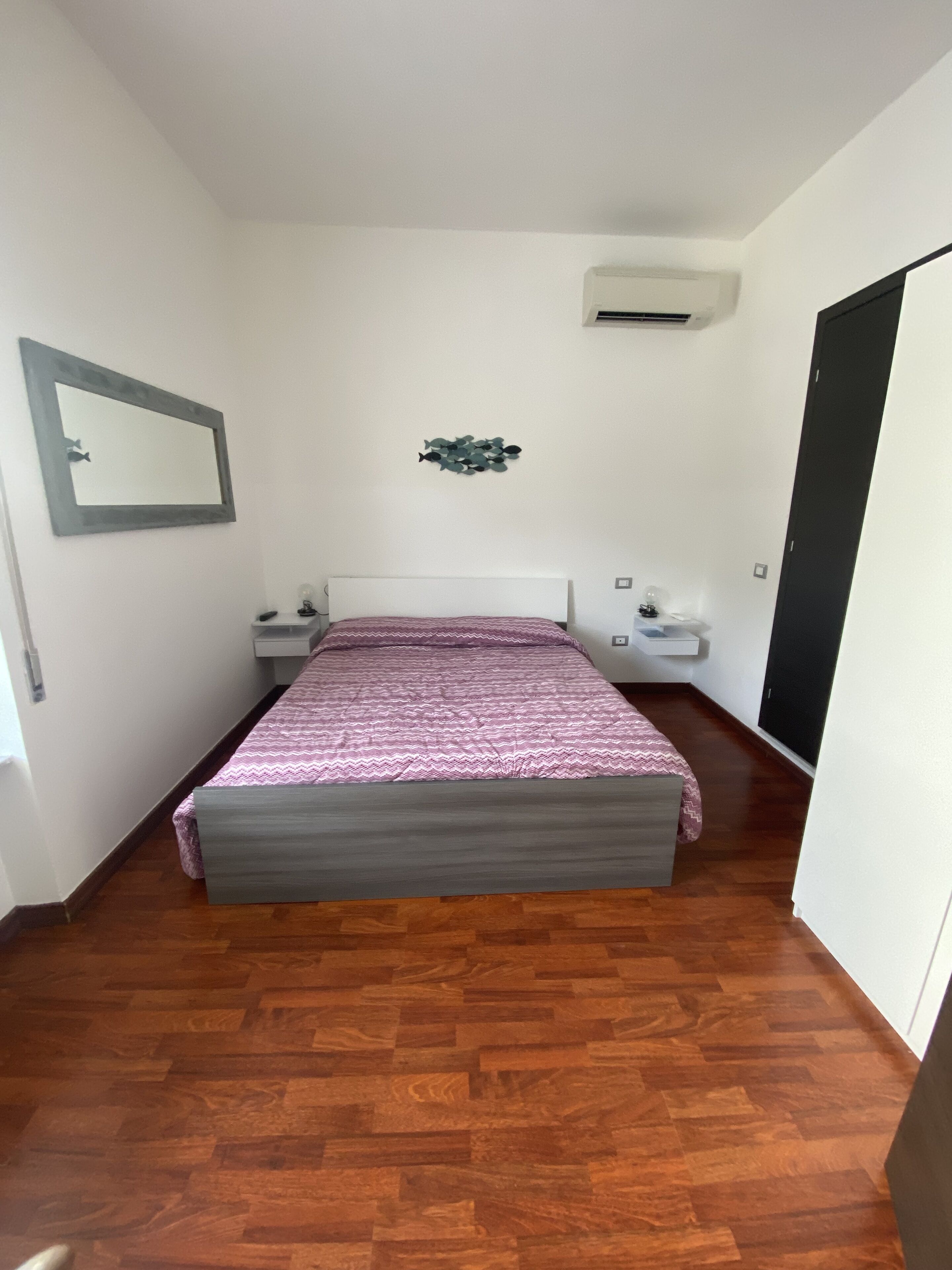 Een slaapkamer met een bed, nachtkastjes, een spiegel en een airconditioning.