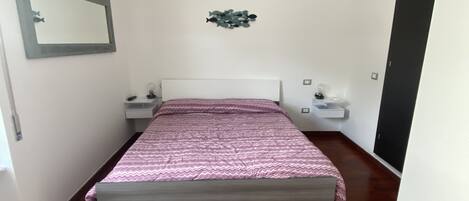 A bedroom with a bed, bedside tables, a mirror, and an air conditioning unit.