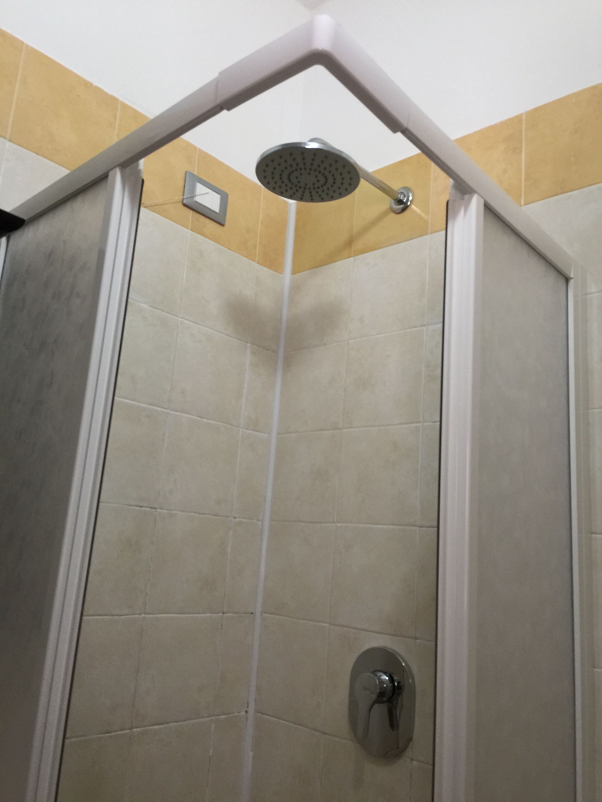 Cabina de ducha con ducha de esquina, paredes con azulejos y panel de control.