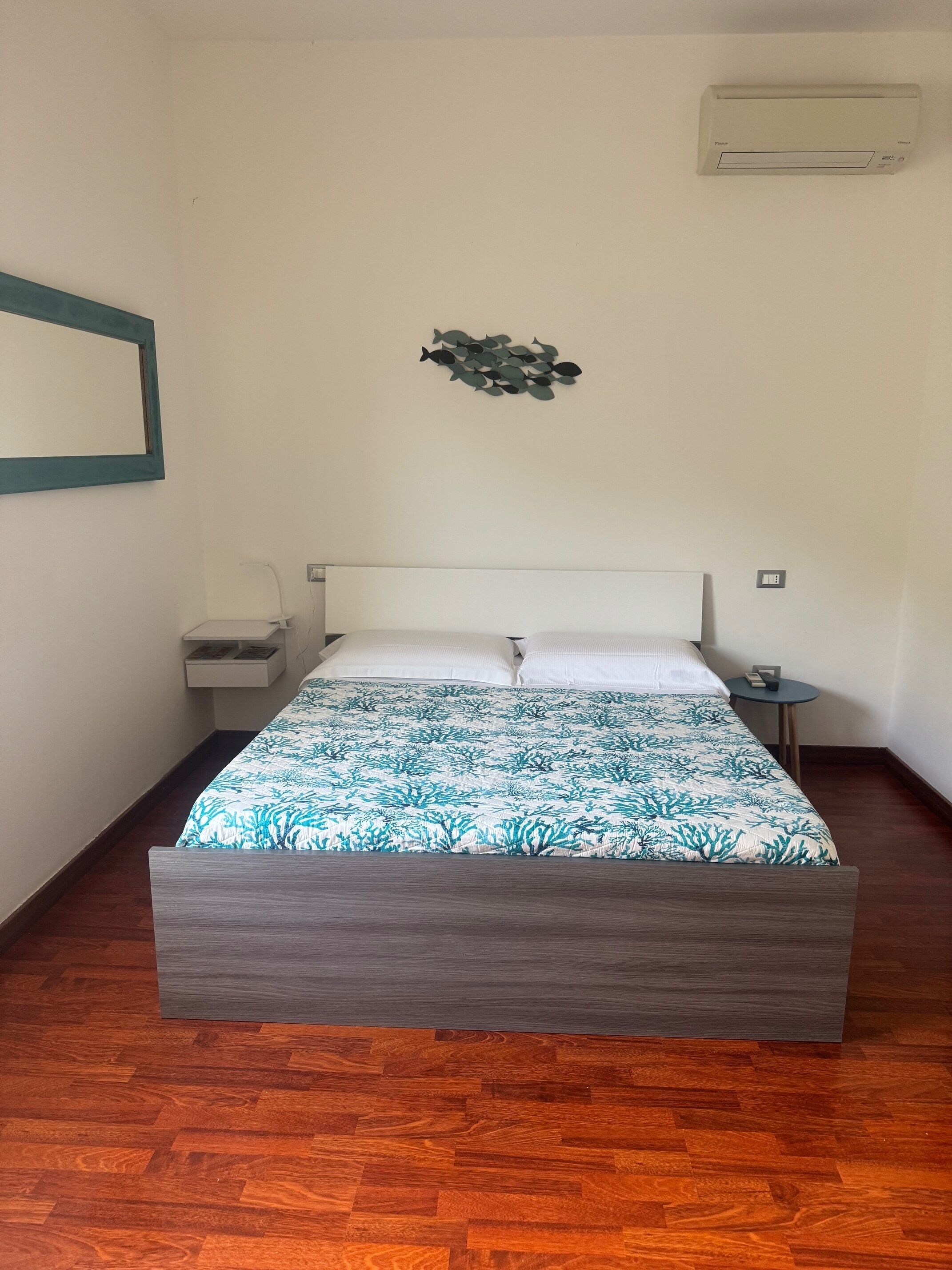 A bedroom with a bed, a nightstand, a wall-mounted air conditioner, and a wall art piece.