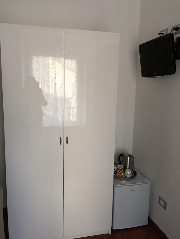 Un armario blanco con dos puertas, un refrigerador pequeño y un televisor de pantalla plana montado en la pared.