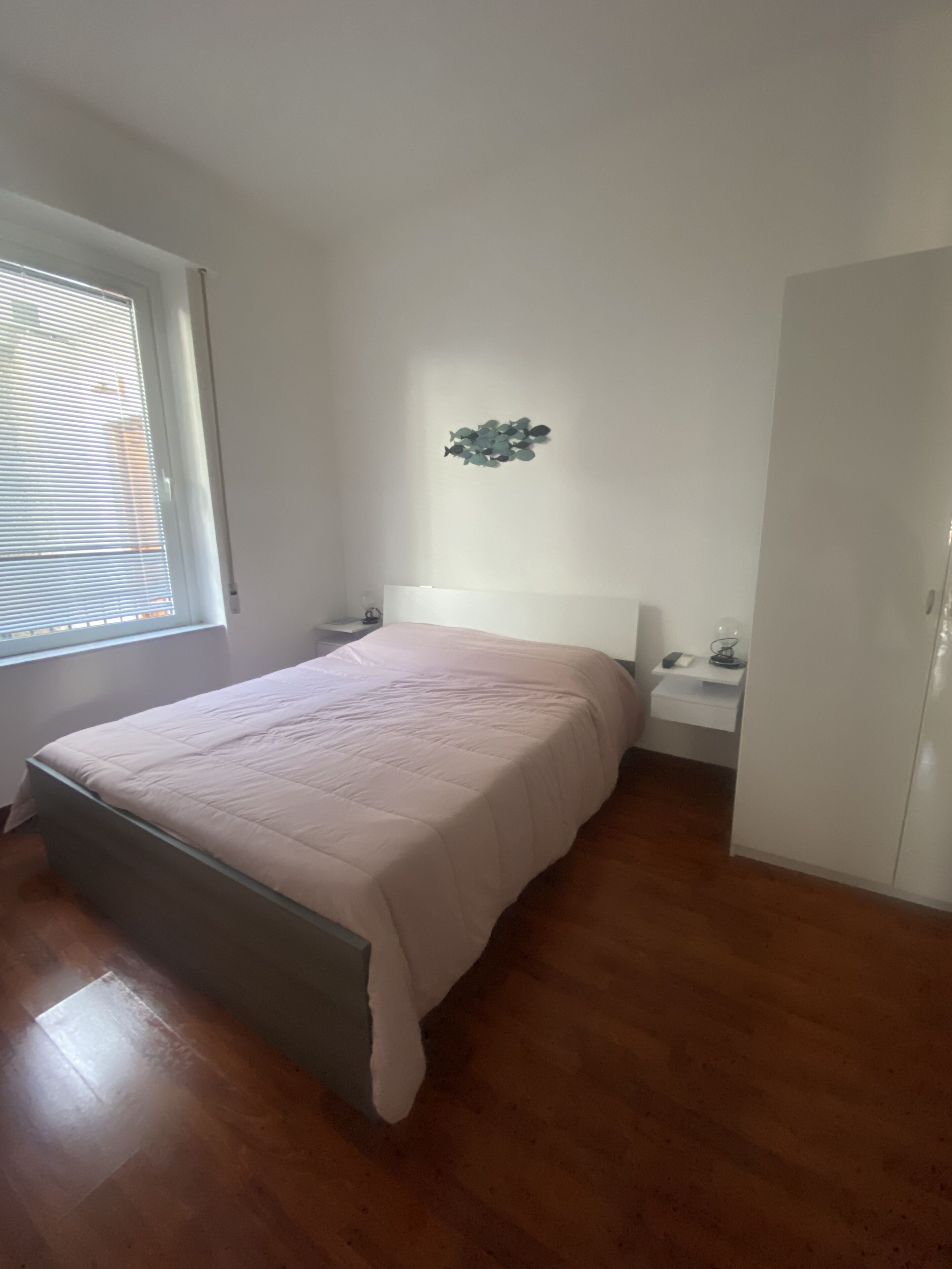 Un dormitorio con cama, mesita de noche, armario y ventana con persianas.