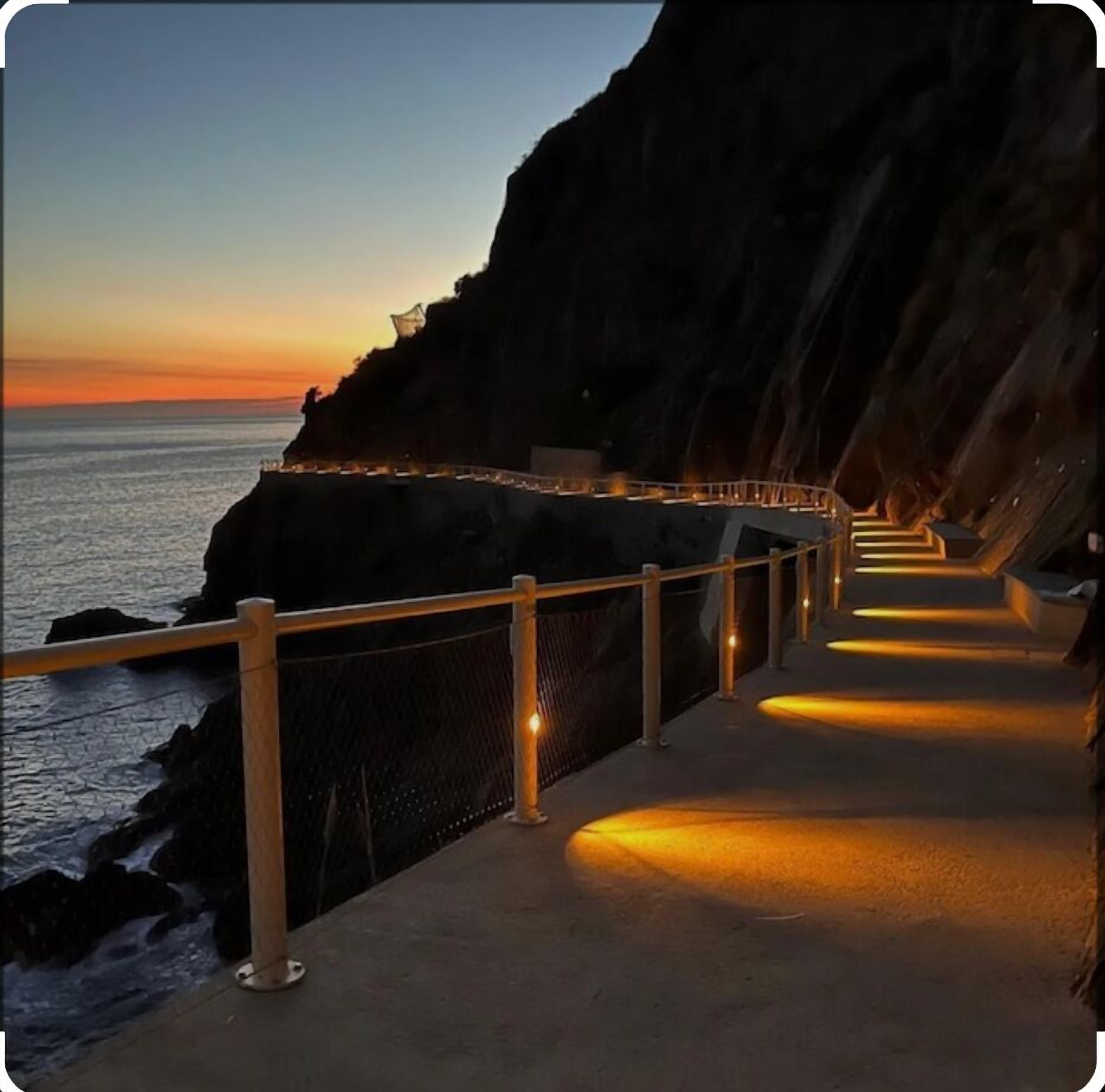 Une promenade en bord de mer, dotée d’une rambarde, qui mène à une falaise surplombant l’océan.