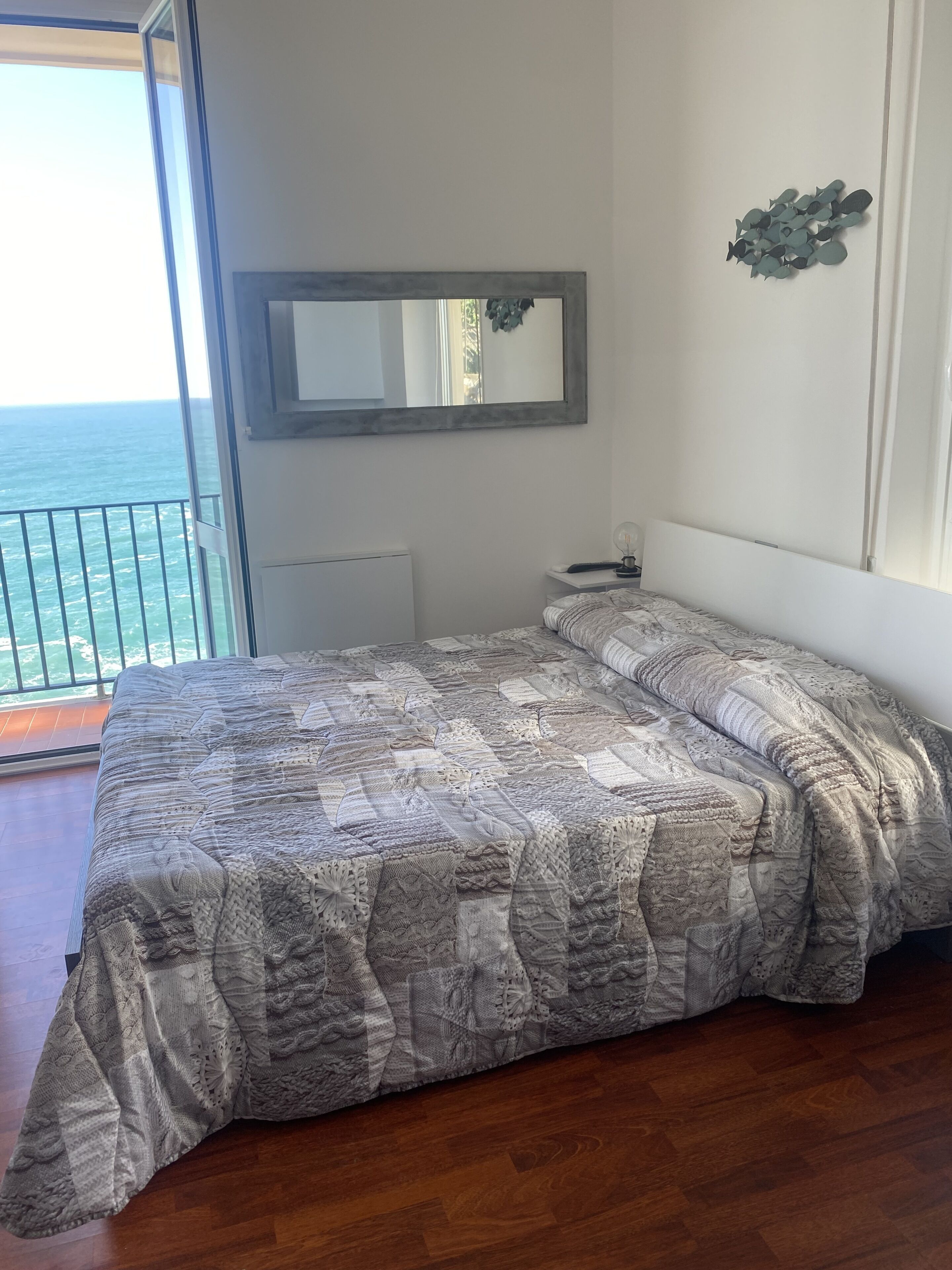 Un dormitorio con una cama grande, una mesita de noche, un espejo y vista al océano.