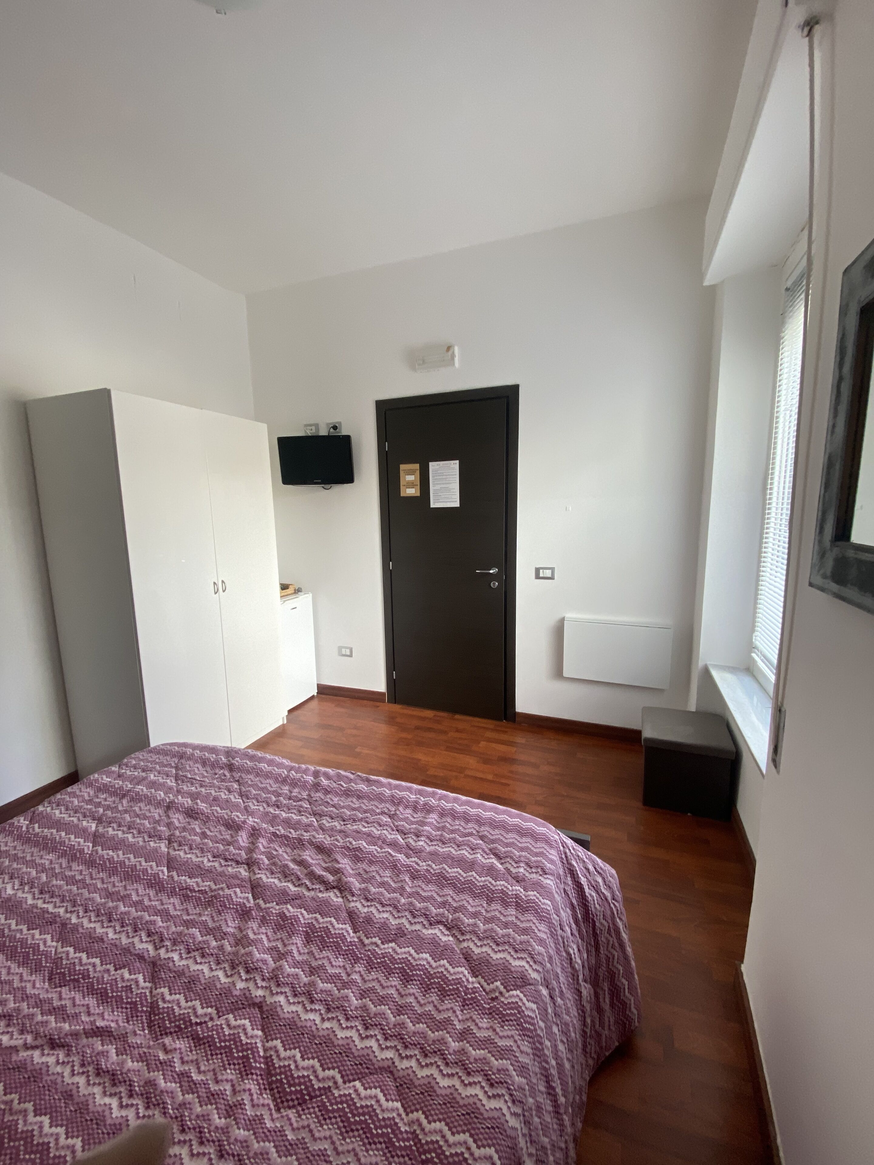Een slaapkamer met een bed, kledingkast en een deur met een bordje.