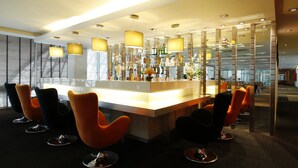 Zona de bar moderna con barra central, diversas opciones de asientos e iluminación ambiental.
