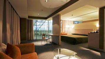 Ein modernes Hotelzimmer mit Glastrennwand, einer Couch, einem kleinen Tisch, einem Bett, einem Schreibtisch und einer Küchenzeile.