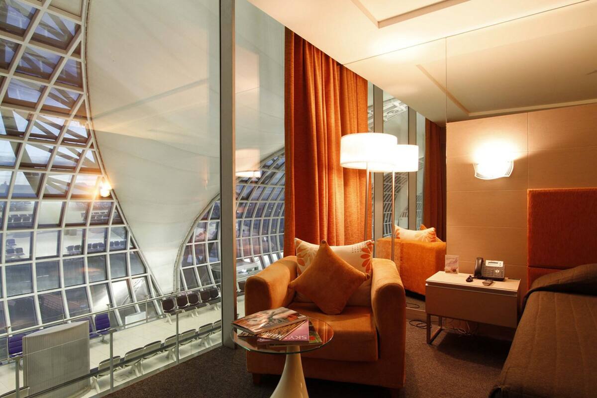 A hotel room with a glass wall, a sofa, a small table, and a nightstand.