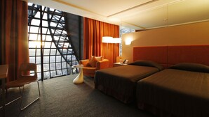 Habitación de hotel con un ventanal grande, un sofá, dos camas y una mesita.