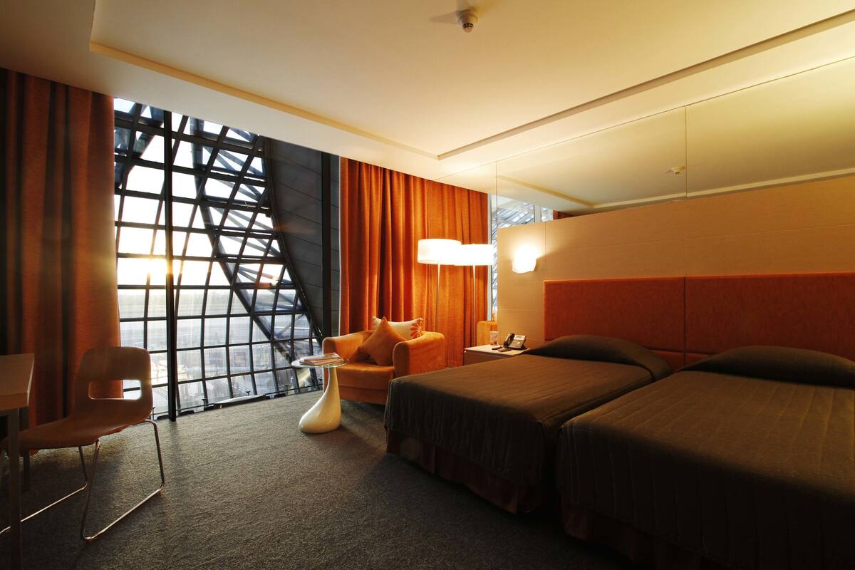 A hotel room with a large window, a sofa, two beds, and a small table.