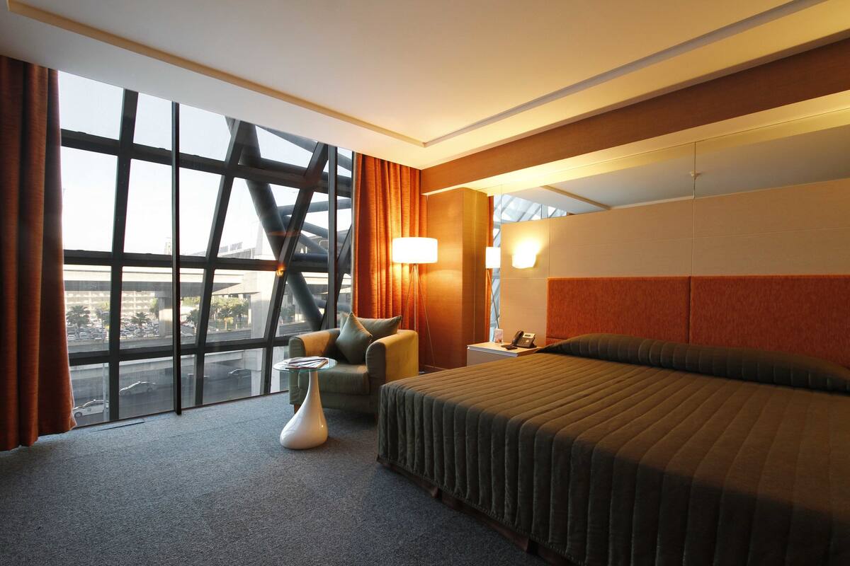 A hotel room with a large bed, a chair, a small table, and a nightstand.