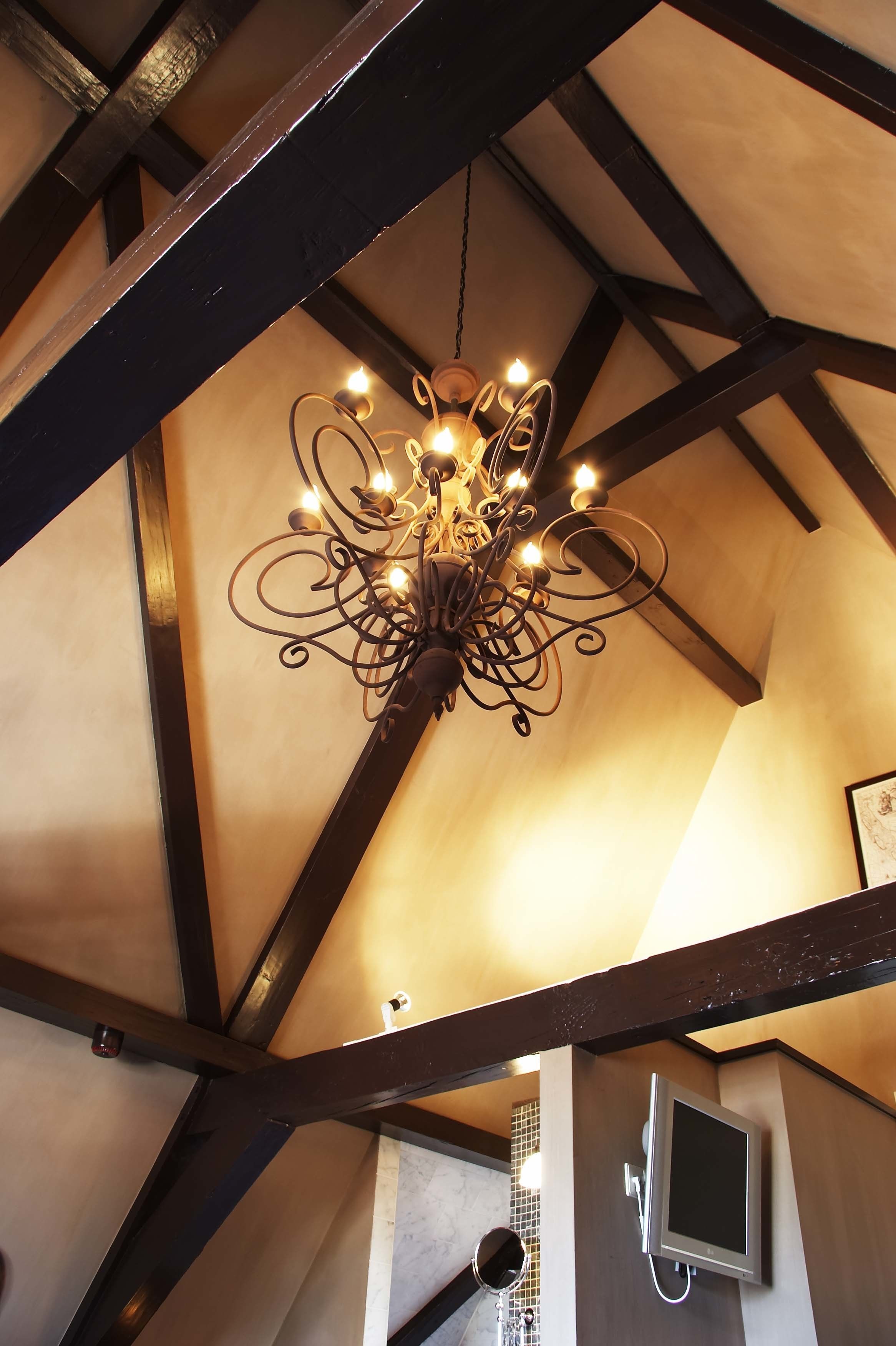 Un lustre composé de plusieurs ampoules suspendues à un plafond sombre, et soutenu par des poutres en bois.
