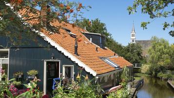 A traditional house with a sloped roof, a visible chimney, and a small garden with flowers and plants.