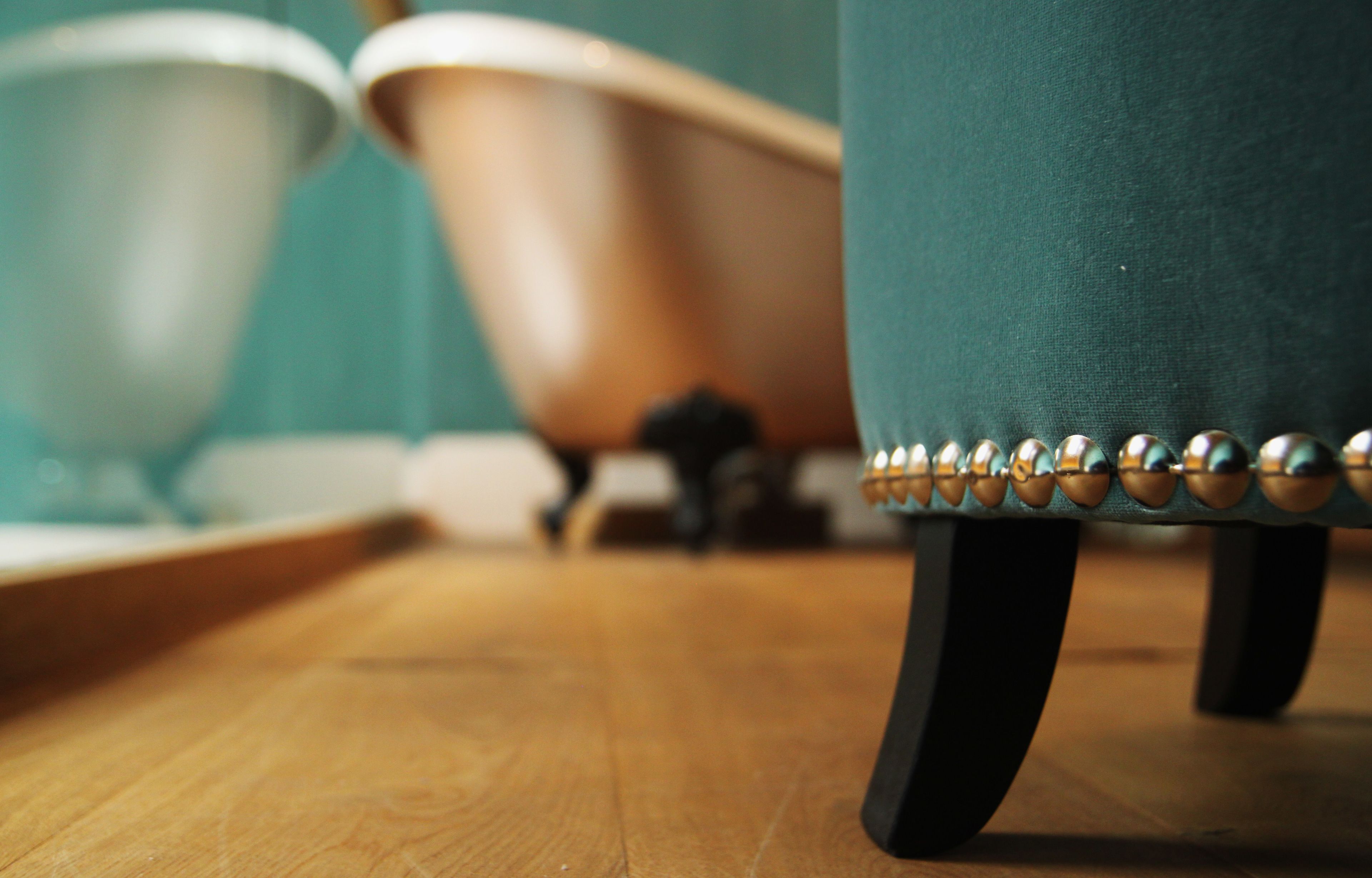 Une vue rapprochée d’un fauteuil recouvert d’un tissu de couleur turquoise, agrémenté de détails métalliques et doté de pieds noirs, posé sur un plancher en bois.