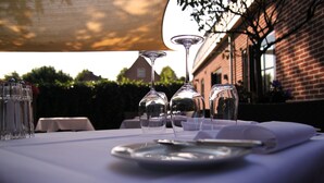A table set for dining with wine glasses and a plate, set against a brick building and trees. - Suitehotel Posthoorn (Monnickendam)