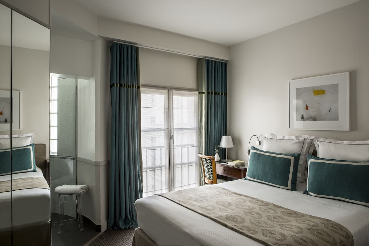 Una habitación de hotel con una cama, un escritorio, una silla, un espejo y una ventana con cortinas.