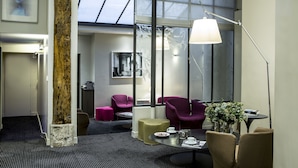Una habitación de hotel moderna con un ventanal grande, un tragaluz, una zona de estar con sillas, una mesa y una lámpara.