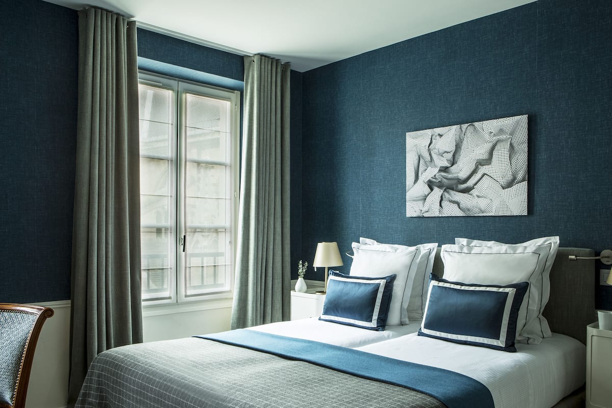 Un dormitorio con una cama grande, dos mesitas de noche, una ventana con cortinas y una obra de arte colgada en la pared.