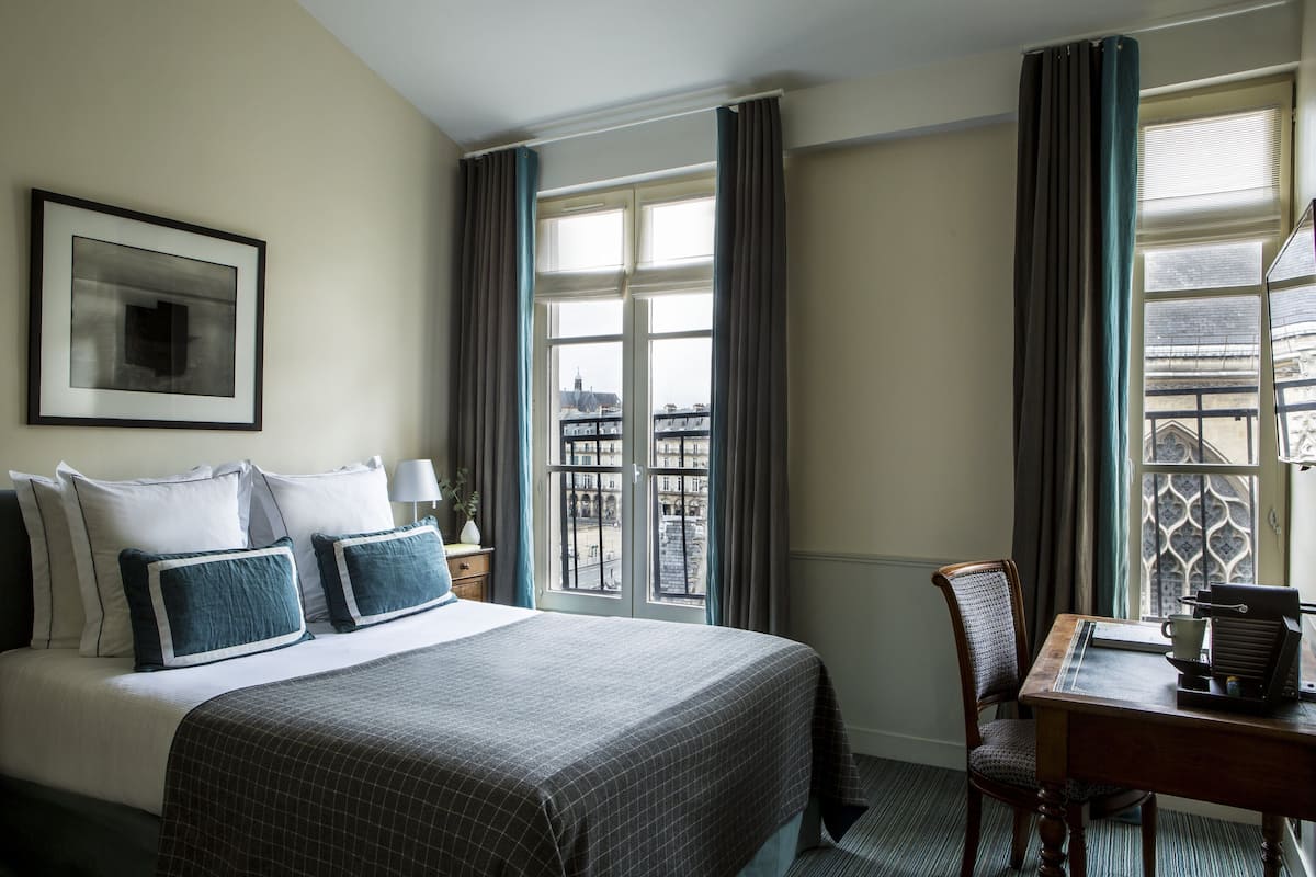 Habitación de hotel con una cama grande, un escritorio con silla, una ventana con cortinas e imagen enmarcada en la pared.