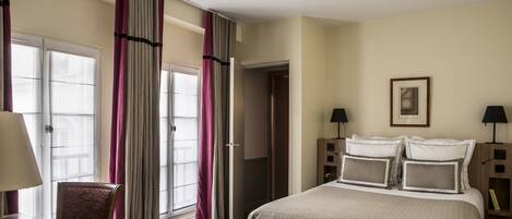 Een hotelkamer met een bed, twee nachtkastjes, een stoel, een raam met gordijnen en een deur.