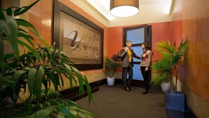 Un hall d’hôtel doté d’un grand mur en bois orné d’un monogramme, de plantes en pot et d’un comptoir d’accueil.