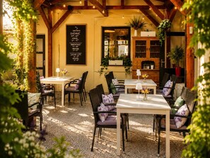 Um café ao ar livre com mesas e cadeiras, um cardápio em lousa e vigas de madeira.