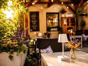 Mesa com abajur e vaso de flores, rodeada por plantas e um ambiente acolhedor.