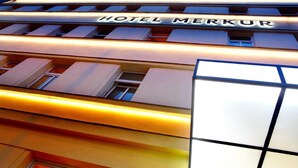 L’extérieur de l’hôtel Merkur, avec son enseigne lumineuse et sa façade moderne.