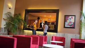 Un hall d’hôtel avec des sièges rouges, un comptoir d’accueil et une horloge au mur.