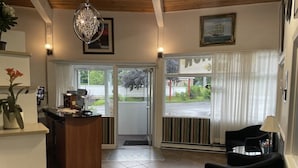 A hotel lobby with a reception desk, a chandelier, a dining area with two chairs, and a large window with curtains.