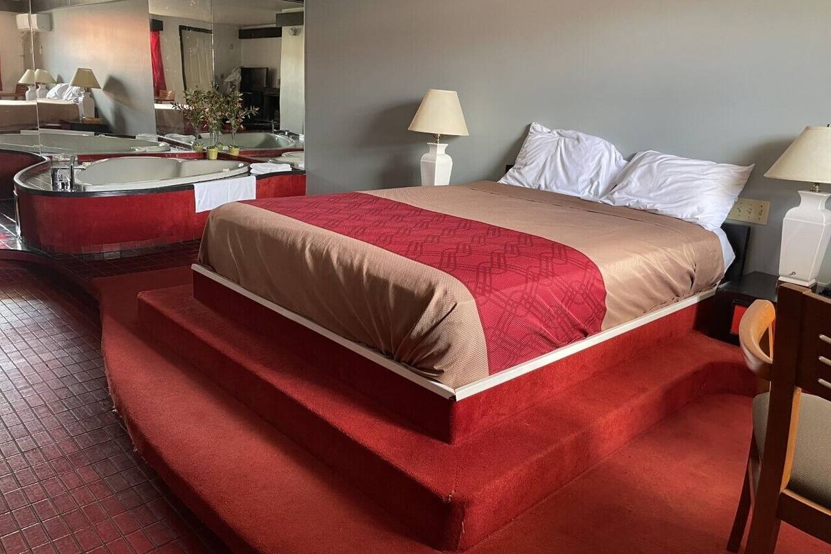 Une chambre d’hôtel avec un grand lit, une zone recouverte d’une moquette rouge, une salle de bain avec un miroir et deux lampes de chevet.