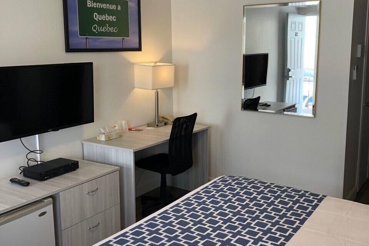 Une chambre d’hôtel équipée d’un lit, d’un bureau, d’une chaise, d’une télévision et d’une pancarte sur laquelle on peut lire : « Bienvenue à Québec ».