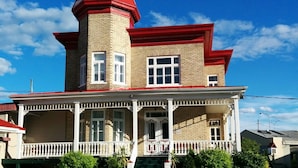 A two-story building with a red roof and a tower, featuring a porch with white railings and potted plants.