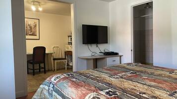 Un dormitorio con cama, escritorio, silla, televisión y puerta que da a un baño.