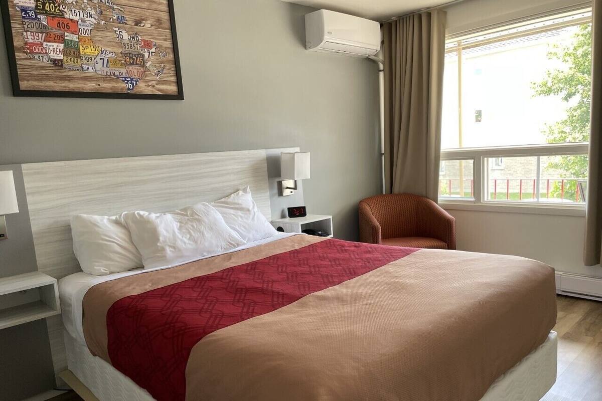 Une chambre d’hôtel avec un grand lit, une table de chevet, une chaise, une fenêtre avec des rideaux et un climatiseur fixé au mur.