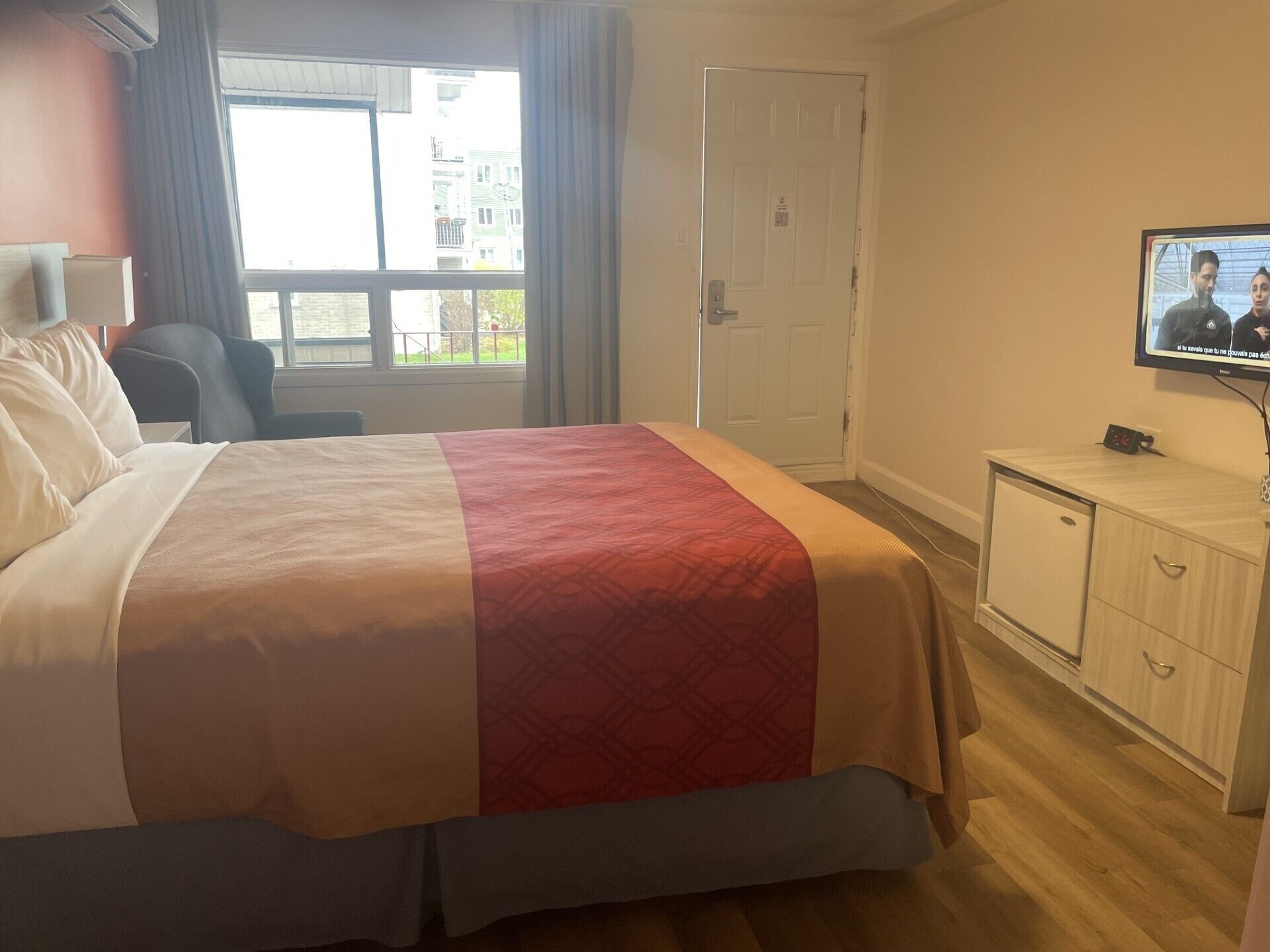 Una habitación de hotel con una cama, televisión, escritorio y armario.