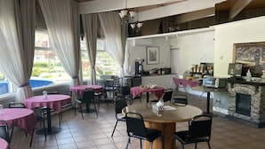 A restaurant with round tables and chairs, a stone fireplace, and a view of the outdoors.